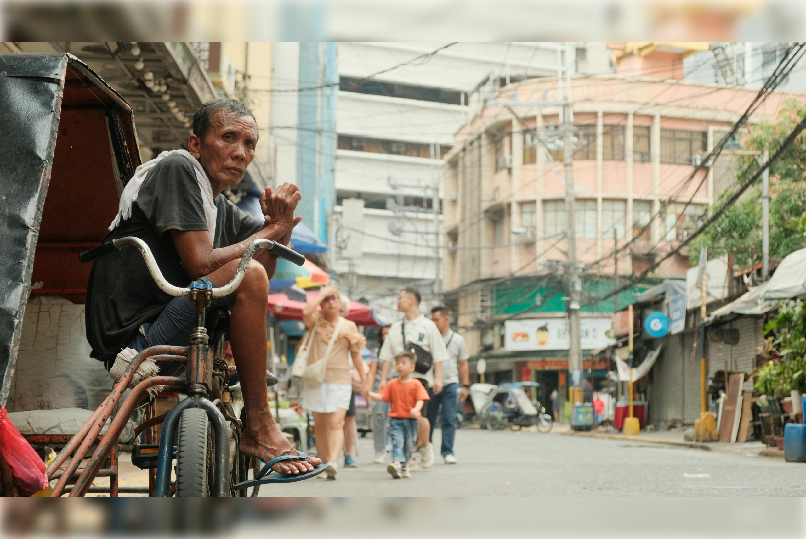 An image of a man on a street sitting on his tricycle, facing the camera